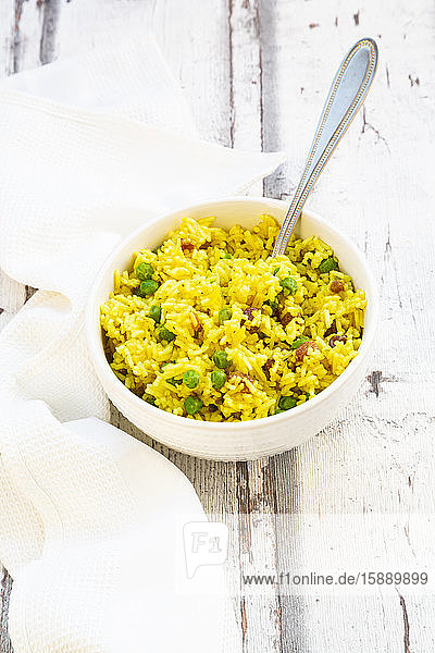 Bowl of pilau rice with green peas raisins and turmeric