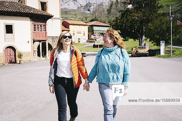 Two happy women with backpacks strolling hand in hand  Valdemurio Reservoir  Asturias  Spain