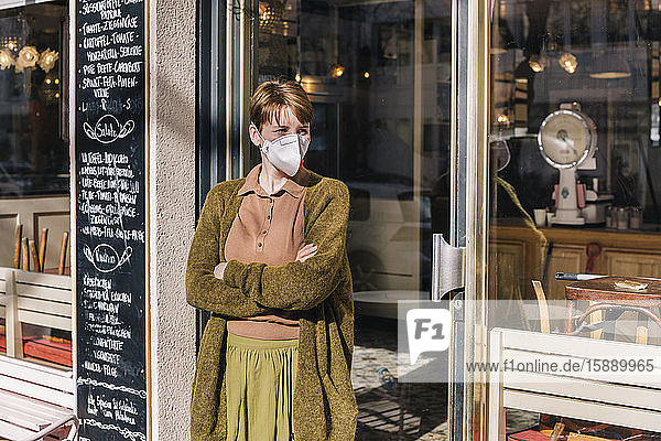 Woman wearing mask standing in front of her closed restaurant
