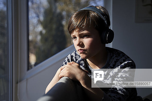 Portrait of pensive boy listening music with headphones while looking out of window