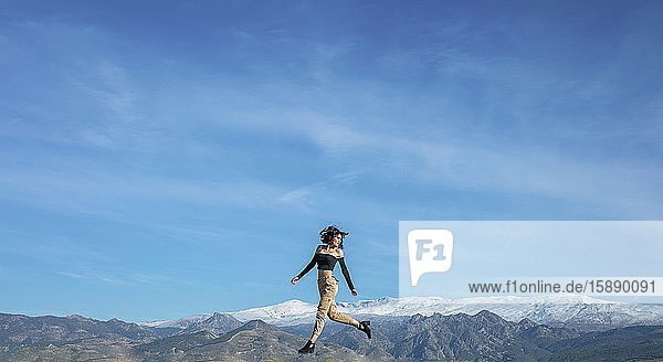 Frau springt mit Bergkette im Hintergrund