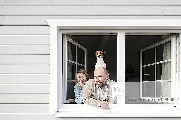 Couple with dog leaning out of window of their house