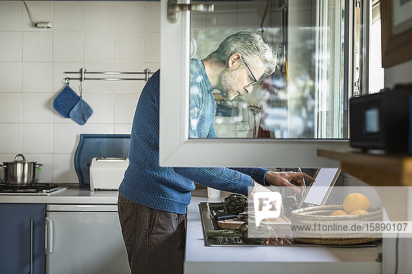 Erwachsener Mann bereitet Artischocke in seiner Küche mit Hilfe eines digitalen Tabletts zu