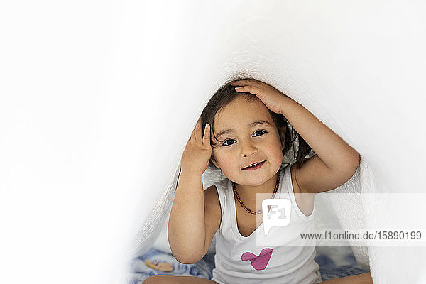 Portrait of little girl hiding under blanket