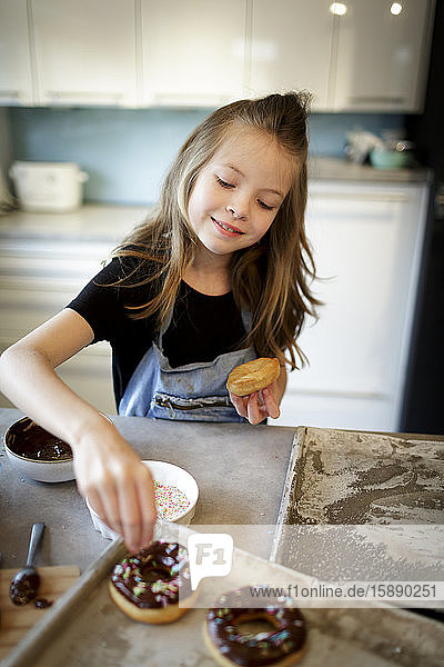 Porträt eines lächelnden Mädchens  das hausgemachte Krapfen mit Zuckergranulat dekoriert