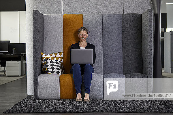 Smiling businesswoman using laptop in office cubicle