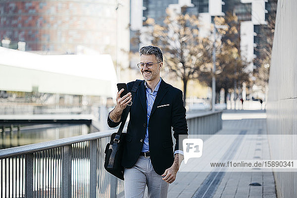 Smiling gray-haired businessman walking in the city using cell phone