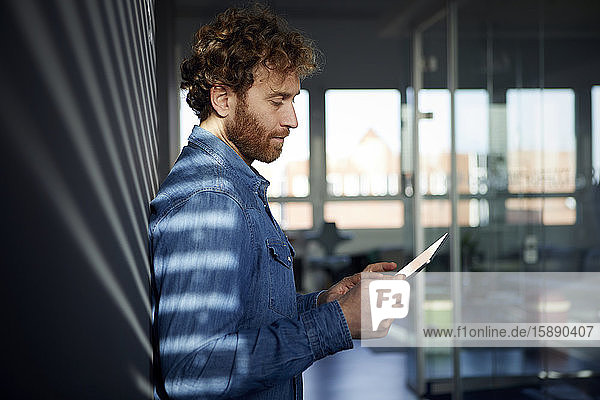 Gelegenheitsunternehmer  der sich im Büro mit einem Tablett an eine Wand lehnt