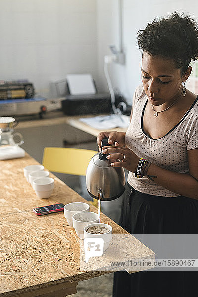 Frau  die in einer Kaffeerösterei arbeitet und heißes Wasser in Kaffeetassen gießt