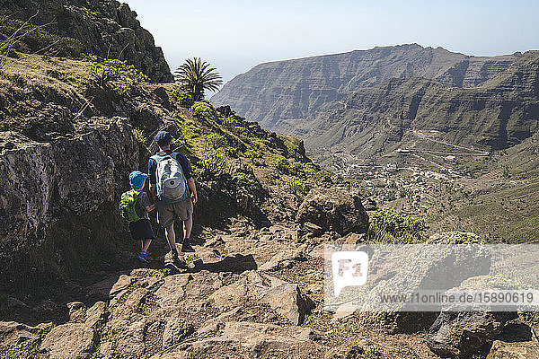 Rückenansicht von Vater und kleinem Sohn mit Rucksäcken auf einem Wanderweg in den Bergen  La Gomera  Kanarische Inseln  Spanien