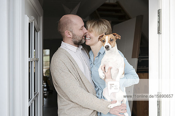 Glückliches Paar mit Hundeküssen am Eingang ihres Hauses