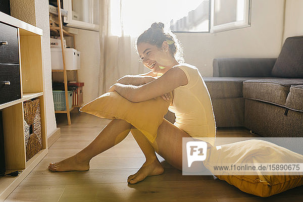 Lachende junge Frau  die zu Hause im Sonnenlicht auf dem Boden sitzt