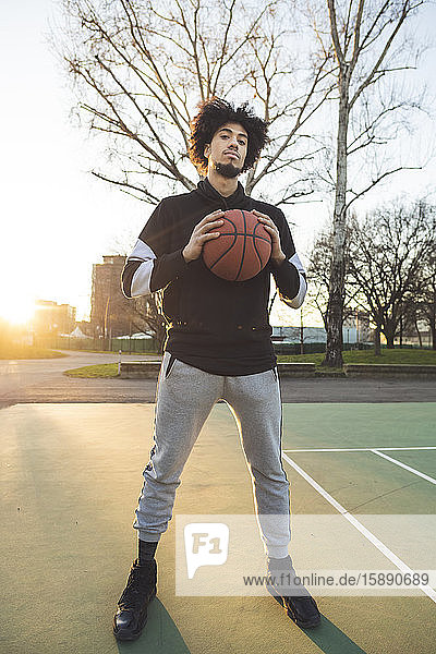 Porträt eines Basketballspielers  der bei Sonnenuntergang auf dem Platz steht