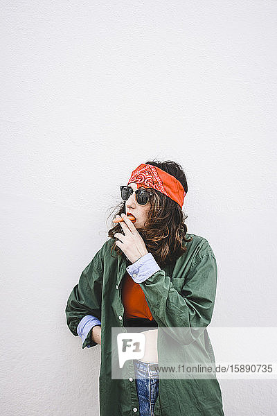 Porträt einer jungen Frau mit Stirnband und Sonnenbrille beim Rauchen von Karotten