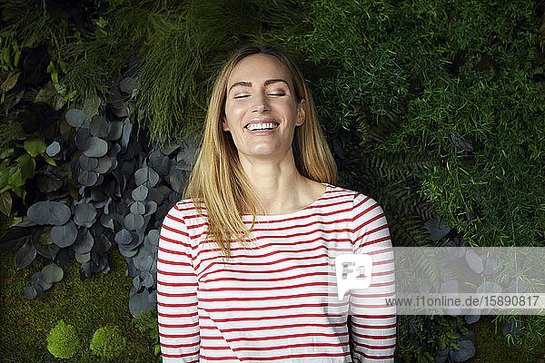 Porträt einer glücklichen Frau mit geschlossenen Augen vor einer grünen Wand
