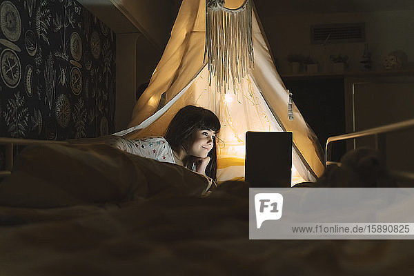 Lächelndes Mädchen liegt mit Laptop auf dem Bett