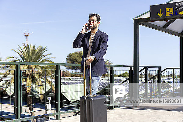 Geschäftsmann am Telefon steht mit Einkaufswagen auf der Dachterrasse eines Flughafens
