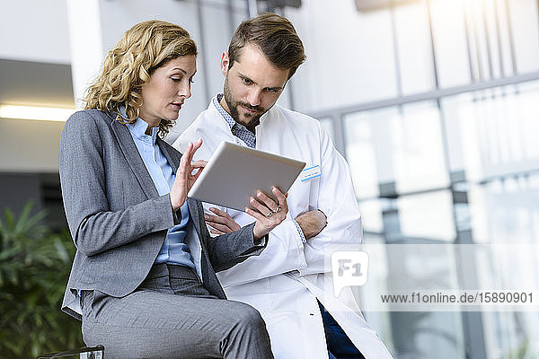 Geschäftsfrau mit Tablette und Arzt im Gespräch im Krankenhaus
