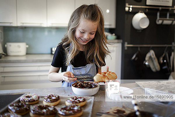 Portrait of smiling girl garnishing home-baked pastry with chocolate icing