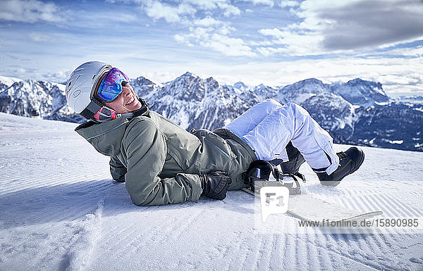 Lächelnde Frau sitzt mit Snowboard auf dem Aussichtspunkt und schaut in die Kamera