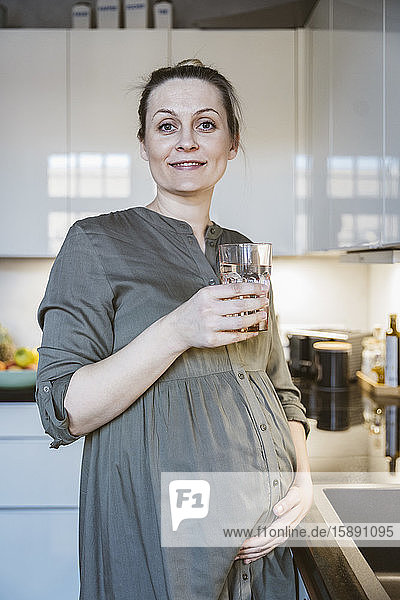 Porträt einer schwangeren Frau  die zu Hause in der Küche ein Glas Wasser hält