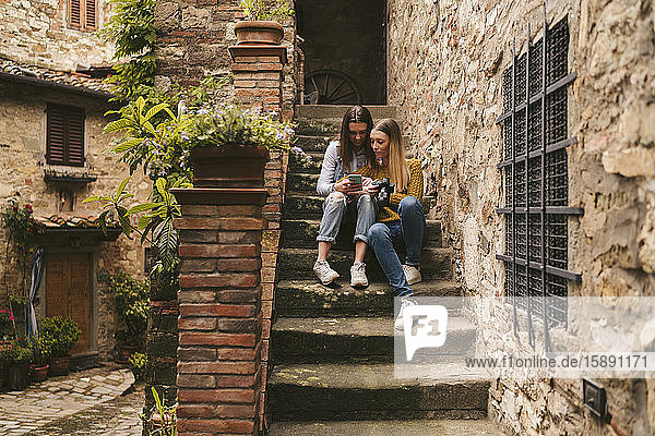 Two young women sitting on stairs looking at smartphone  Greve in Chianti  Tuscany  Italy