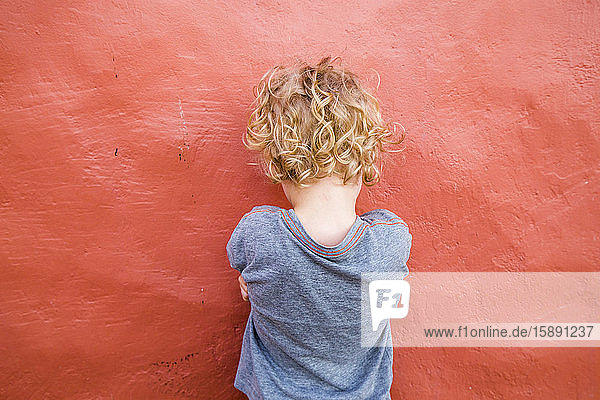 Back view of little boy standing in front of red wall