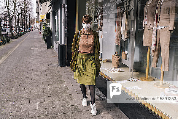 Frau mit Maske geht an einem Bekleidungsgeschäft in der Stadt entlang