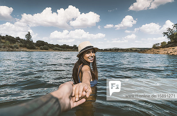 Porträt einer glücklichen jungen Frau  die in einem See badet und die Hand ihres Freundes hält