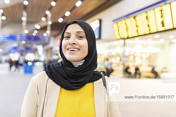 Porträt einer lächelnden jungen Frau mit Hidschab am Bahnhof