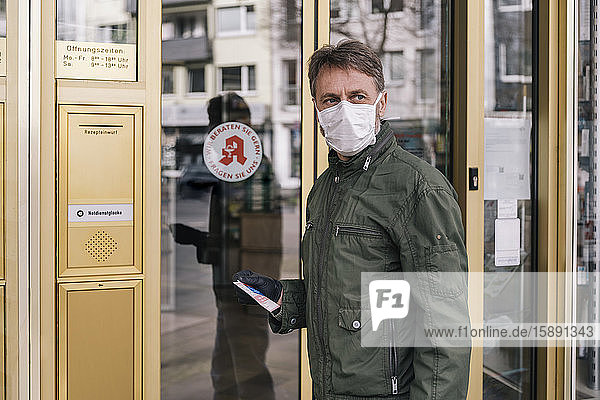 Mann mit Maske wartet mit einem Rezept vor der Apotheke