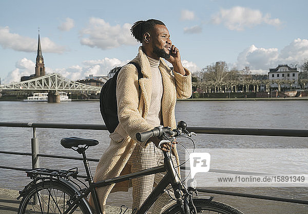 Stylish man with a bicycle talking on the phone on riverbank  Frankfurt  Germany