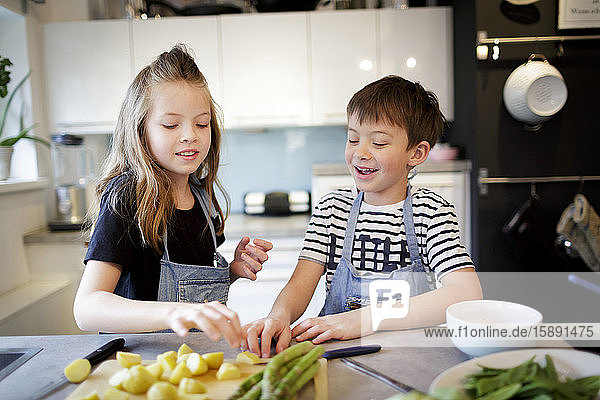 Porträt eines Mädchens und ihres kleinen Bruders bei der Zubereitung von Gemüse in der Küche