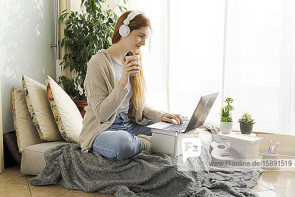 Junge Frau mit Kopfhörern und Laptop zu Hause