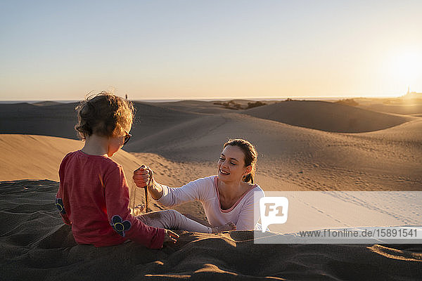 Mother and daughter playing with sand in dunes at sunset  Gran Canaria  Spain