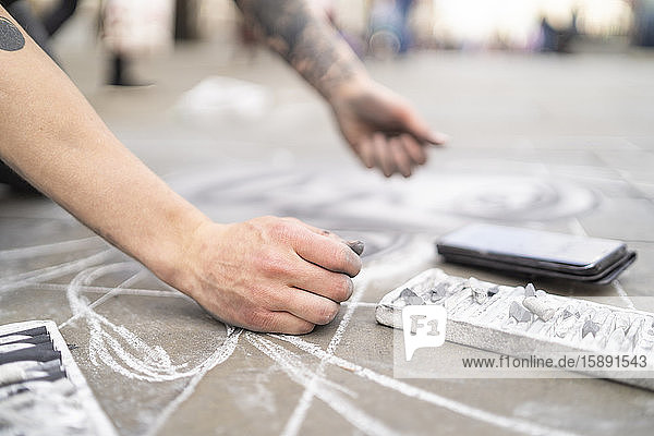 Straßenkunst  Bürgersteigkünstler  der auf dem Bürgersteig zeichnet und ein Smartphone benutzt