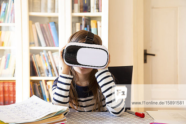Mädchen  das zu Hause am Tisch sitzt und eine Virtual-Reality-Brille benutzt
