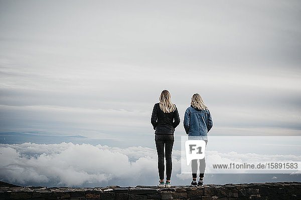 Rückansicht von Freundinnen  die auf idyllische Wolkenlandschaft blicken  während sie am Vulkan Haleakala stehen  Hawaii  Maui  USA