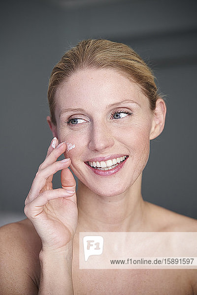 Portrait of happy beautiful woman applying cream on her cheek