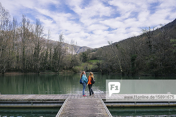 Two happy women with backpacks standing on jetty  Valdemurio Reservoir  Asturias  Spain