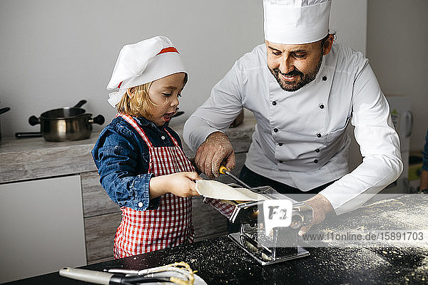 Vater und Tochter machen hausgemachte Nudeln mit der Nudelmaschine in der heimischen Küche