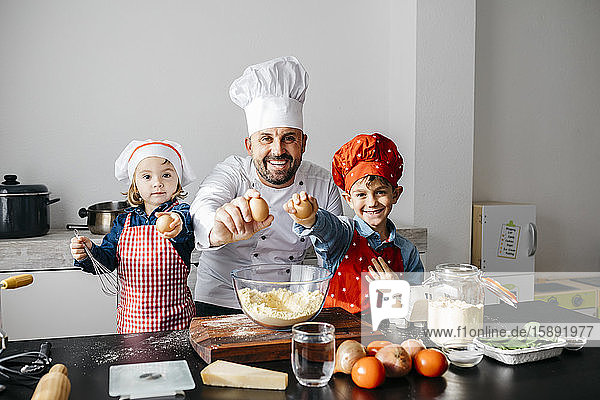 Porträt eines Vaters mit zwei Kindern  die zu Hause in der Küche Teig zubereiten