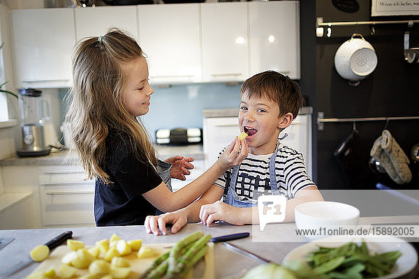 Mädchen  das seinen kleinen Bruder in der Küche mit Kartoffeln füttert