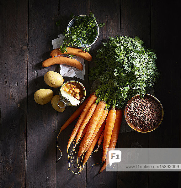 Ein Bündel Karotten,  Würste,  Petersilie,  Kartoffeln,  Linsensuppe in Dosen und eine Schüssel Linsen