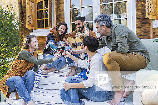 Freunde spielen Musik auf der Gitarre und trinken Wein vor einer Hütte auf dem Land