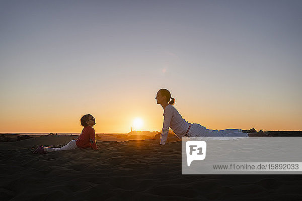 Mutter und Tochter praktizieren Yoga in Sanddünen bei Sonnenuntergang  Gran Canaria  Spanien