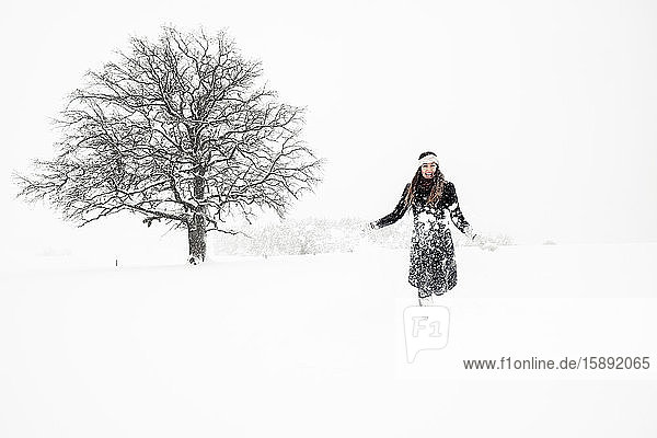 Happy young woman throwing snow in winter landscape