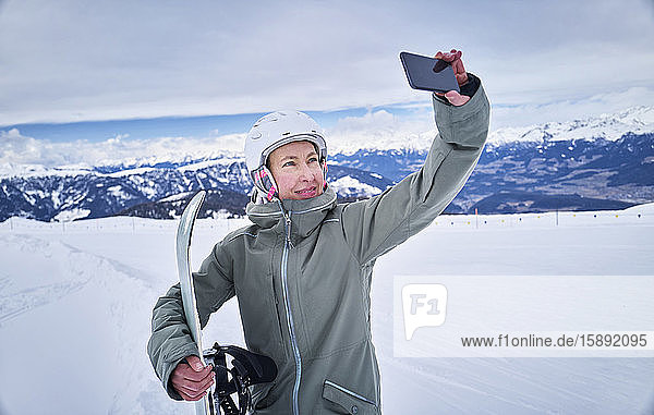 Lächelnde Snowboarderin beim Selbstfahren mit ihrem Smartphone
