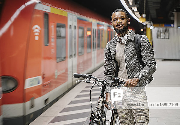 Stylish man with a bicycle and headphones in a metro station