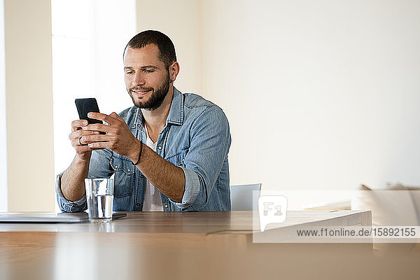 Lächelnder junger Mann zu Hause  der sein Smartphone überprüft